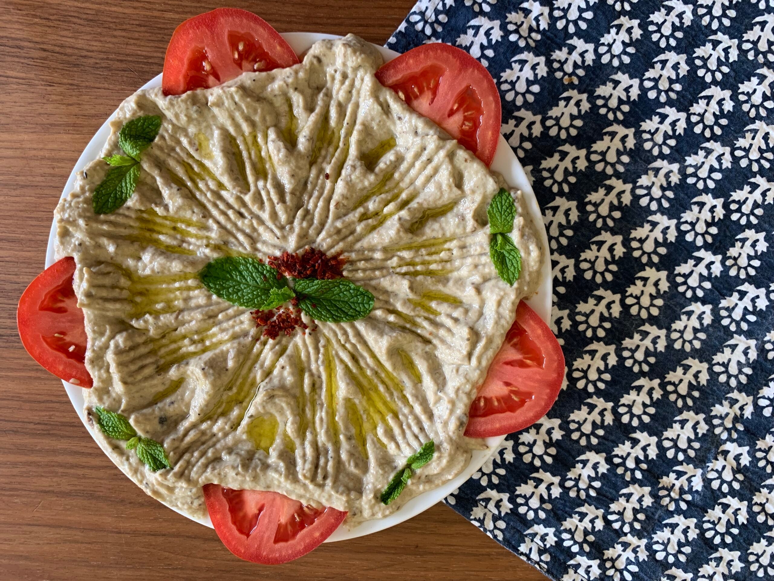 A decorative cloth and a plate of soft mutabal with mint, olive oil, parsley, and chili flake garnishes.