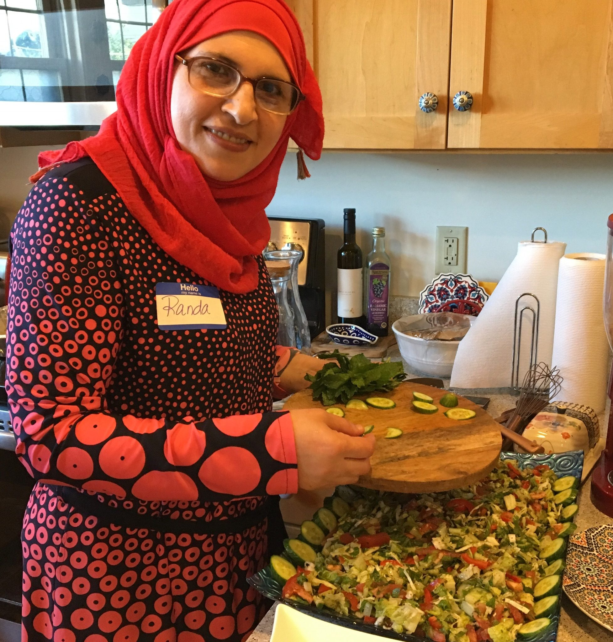 Chef Randa poses with ingredients, parsley, tomatoes and spices on a wood table.