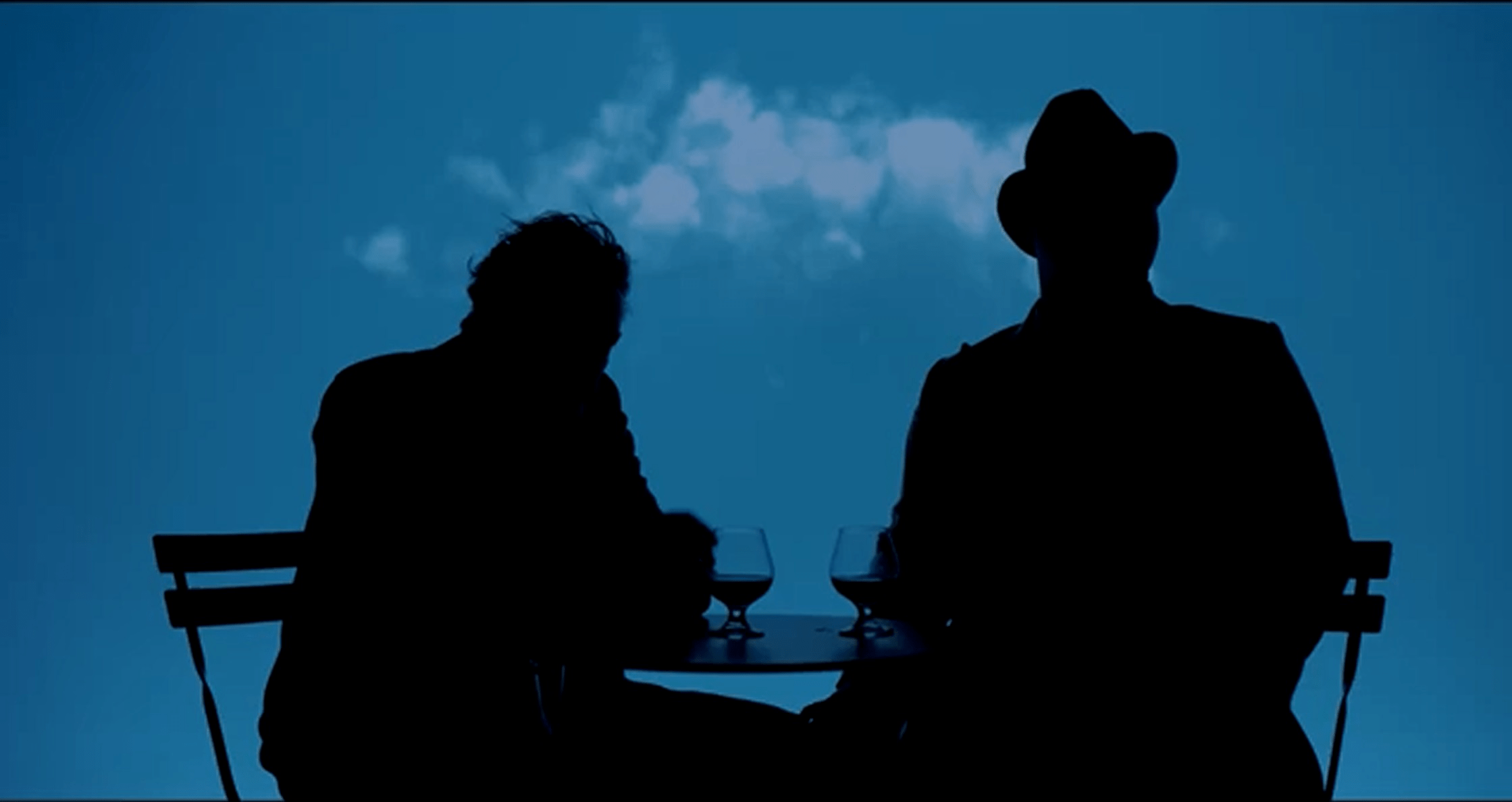 Silhouettes of two people sitting at a small table with drinks against a blue cloud background.